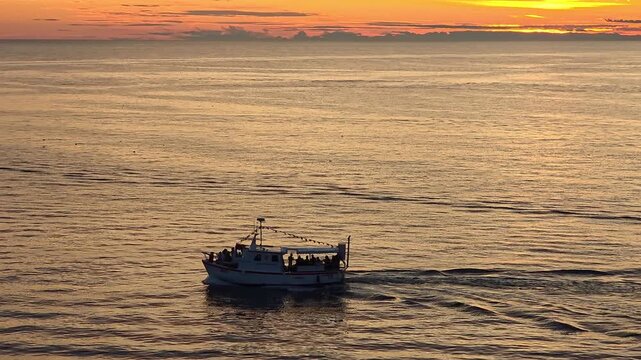 Boat with passengers sailing on Adriatic Sea during golden sunset in Rovinj Croatia, dramatic horizon with warm colors reflecting on water creating travel atmosphere