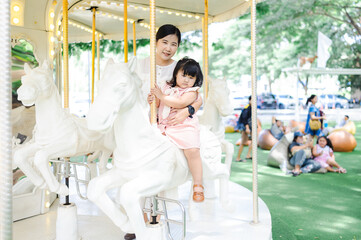 Obraz premium Asian mother and daughter riding a carousel in an amusement park.