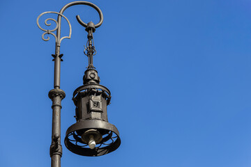 Ornate vintage street lamp, featuring intricate wrought iron details against a clear blue sky, symbolizing classic urban architecture and timeless city lighting
