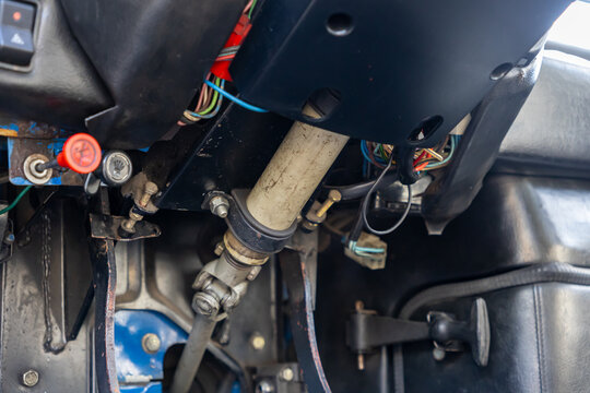 Exposed electrical wiring, steering column, and mechanical controls visible under an old car dashboard, highlighting automotive repair and maintenance