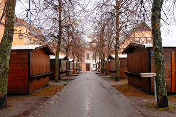 Wooden stalls line a charming street in the heart of the city, adorned with Christmas decorations, inviting visitors to enjoy festive treats and holiday shopping.
