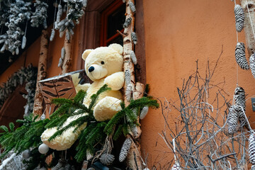 Colorful Christmas decorations enhance the festive atmosphere at a city Christmas market, featuring a large teddy bear surrounded by evergreen plants and pine cones.