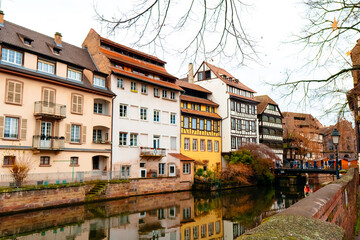 Festive lights and decorations line the riverbanks in Colmar as historic buildings reflect in the calm water, creating a serene holiday atmosphere during winter.