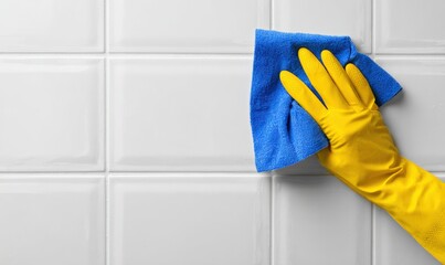 Cleaning a white tiled wall with a blue cloth and yellow glove