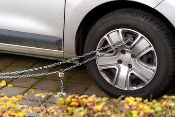 Car wheel locking with metal chain and padlock, preventing movement. Theft protection or as penalty for illegal parking. Personal vehicle security. DIY safety methods for property protection