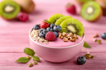 A vibrant bowl of yogurt topped with fresh berries, kiwi slices, granola, and nuts, set against a pink wooden background.