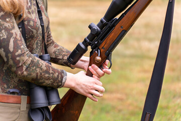 Female dressed for hunting examines her rifle outdoors. Blending into nature. Stealth and patience. Hunting as lifestyle for woman. Women in traditionally male roles. Wilderness survival skills