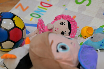 Colorful children's toys, including a multicolored soccer ball and plush dolls, are scattered on a baby mat. The mat features playful designs and letters.