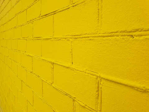 Textured brick wall yellow side view, with uneven surface. Rough and grunge texture. Brick painted with yellow paint. Uneven, sloppy brickwork