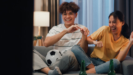 Asian new marriage couple sit on sofa excited cheering watching football sport game on television...
