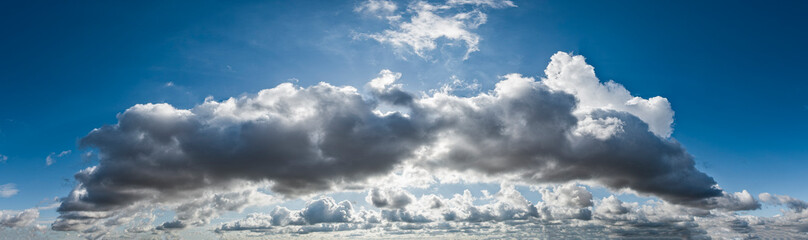 Fototapeta premium Panoramafoto des dramatischen, kontrastreichen Wolkenhimmels mit durch die Wolken scheinenden Sonnenstrahlen der dahinter stehenden, verdeckten Sonne