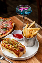 Enjoying a delicious hot dog and fries. A hot dog topped with condiments sits on a plate beside a serving of fries and a colorful drink at a restaurant.