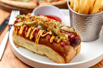 Tasty hot dog, fries included. A tasty hot dog topped with mustard and jalapenos served alongside crispy fries on a casual dining table.