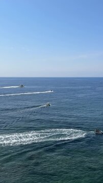 Several motorboats sail through the waves on a sunny day.