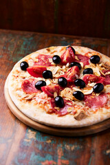 Pizza with ham, salami, tomatoes and mozzarella cheese. Rustic wooden background. Soft focus. Close up.	