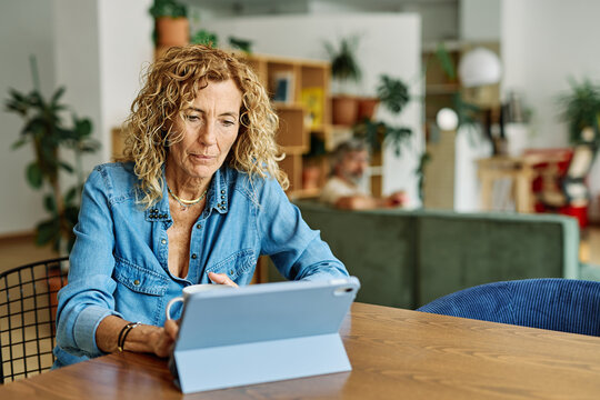 Portrait of a mature senior woman a businesswoman using tablet laptop working from home having a meeting online drinking coffee or tea, home office, or a student learning, or mature woman surfing net
