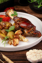 Juicy grilled chicken leg served with roasted baby potatoes, cauliflower, fresh tomato slice and parsley garnish on rustic table