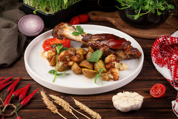 Juicy grilled chicken leg served with roasted baby potatoes, cauliflower, fresh tomato slice and parsley garnish on rustic table