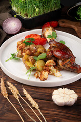Juicy grilled chicken leg served with roasted baby potatoes, cauliflower, fresh tomato slice and parsley garnish on rustic table