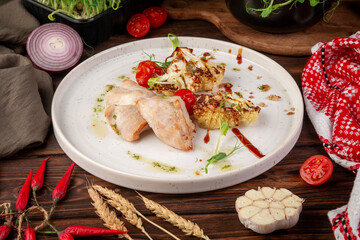 Juicy baked turkey fillet served with roasted cauliflower, cherry tomatoes and herbs on white plate in rustic food styling