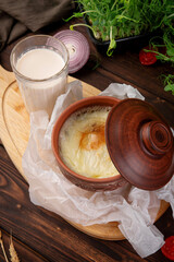 Hot baked casserole with melted cheese crust in clay pot served with glass of fresh milk on wooden board