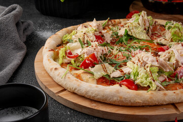 Fresh Caesar pizza topped with sliced chicken breast, lettuce, cherry tomatoes, arugula and grated parmesan on wooden board