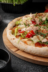 Fresh Caesar pizza topped with sliced chicken breast, lettuce, cherry tomatoes, arugula and grated parmesan on wooden board