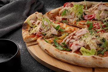 Homemade sliced caesar pizza with chicken breast, lettuce, cherry tomatoes, arugula and parmesan cheese on wooden board