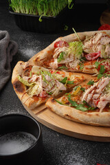 Homemade sliced caesar pizza with chicken breast, lettuce, cherry tomatoes, arugula and parmesan cheese on wooden board