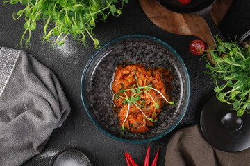 Traditional stewed cabbage in tomato sauce with fresh herbs served in dark ceramic bowl on rustic table
