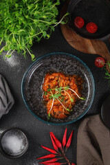Traditional stewed cabbage in tomato sauce with fresh herbs served in dark ceramic bowl on rustic table