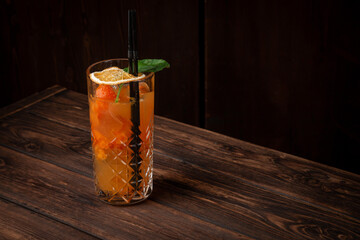 Refreshing highball cocktail with orange juice, basil, ice cubes and dried orange slice in tall crystal glass on wooden table