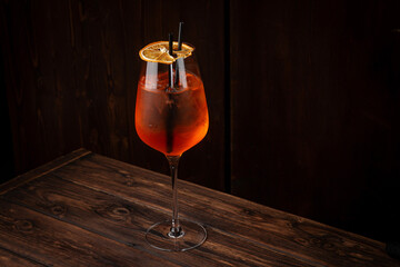 Classic aperol spritz cocktail with prosecco, aperol, soda, ice and dried orange slice in large wine glass on wooden table
