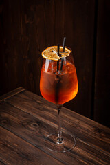 Classic aperol spritz cocktail with prosecco, aperol, soda, ice and dried orange slice in large wine glass on wooden table