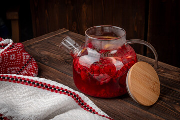 Hot berry fruit tea with fresh raspberry, lemon slices and herbs served in transparent glass teapot on rustic wooden table