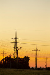 Fototapeta premium Silhouettes of electricity transmission towers against a vibrant sunset sky, illustrating energy infrastructure in a serene landscape.