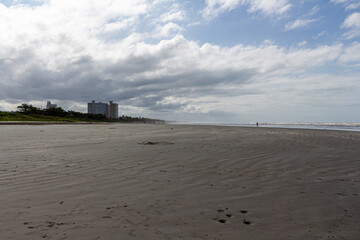 Peru&iacute;be, SP, Brazil - May 31st, 2025: Vast expanse of sand seen from Praia Central Queer with the famous Praia do Canto and Serra do Itatins buildings in the background.