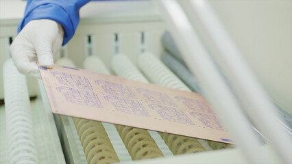 Gloved hand carefully placing printed circuit board onto rollers in high tech electronics manufacturing facility, ensuring quality and precision in production process