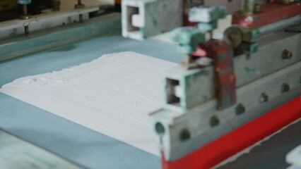 Close up of automated silkscreen printing machine applying white plastisol ink on piece of light fabric, showcasing industrial textile printing process