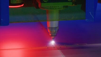 Industrial laser engraving machine cutting a metal plate, emitting red and blue lights, in a...