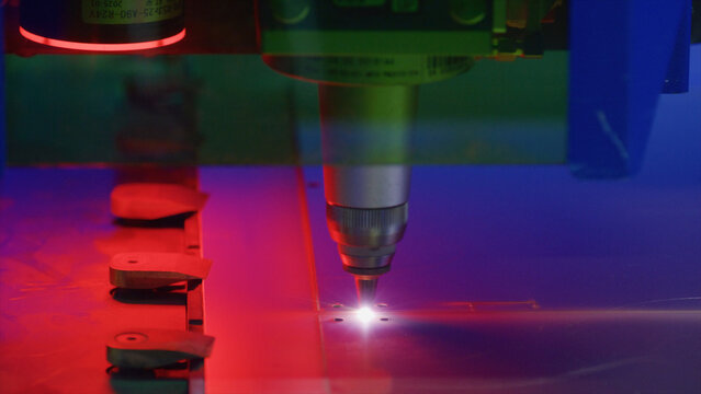 Automated industrial laser engraving process taking place in a factory, featuring vibrant red and blue lights while executing precise cutting and marking operations on metal sheets