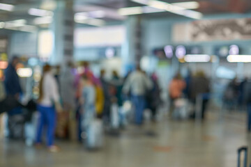 Blurry airport terminal with diverse people and luggage in busy waiting area.
