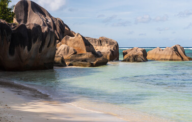 Sandy beach with large granite stones, blue Indian Ocean and blue sky with clouds. La Digue, the Seychelles