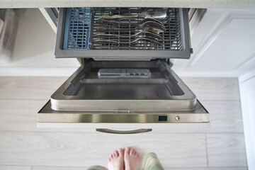 Open dishwasher with clean utensils in modern kitchen viewed from above.