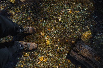 Hiking Boots Standing in Clear Stream Water with Colorful Stones and Pebbles Outdoors Adventure Travel Concept