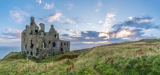 Historische Burgruine Dunure Castle in South Ayrshire, Schottland. Die Festung thront auf einer Klippe über dem Meer, umgeben von Felsen und Gras. Warmes Licht und dramatische Stimmung