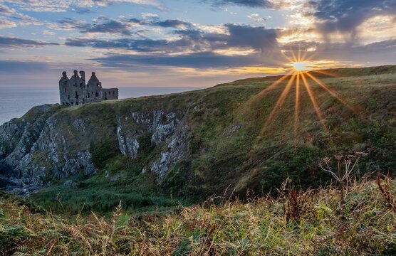 Historische Burgruine Dunure Castle in South Ayrshire, Schottland. Die Festung thront auf einer Klippe &uuml;ber dem Meer, umgeben von Felsen und Gras. Warmes Licht und dramatische Stimmung