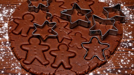 round chocolate cookie dough wooden surface covered powdered sugar several cookie cutters scattered around dough including star man woman child cookie dough appears freshly baked has golden brown