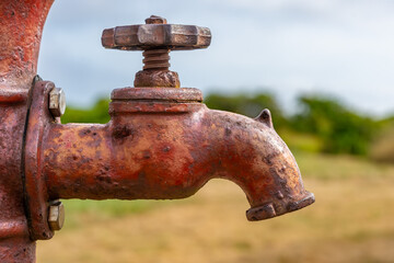 Close up, abstract image of an old, rustic, red well spigot with rust stains on a sunny summer morning. 