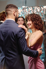 Teen girl smiling while dancing with boy at formal event, holding each other closely, other teenagers visible in background